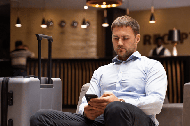 Business man in blue shirt sitting in a hotel reception lobby working on his phone